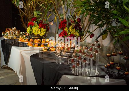 Un élégant buffet de restauration est servi à l'extérieur le soir, avec une variété de hors-d'œuvre salés et de pièces maîtresses florales pour un événement formel. Banque D'Images