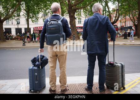 Deux voyageurs attendent avec leurs bagages pour un trajet en taxi sur le trottoir de Sloane Square, le 20 mai 2026, à Londres, en Angleterre. Banque D'Images