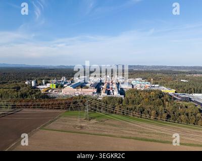 Cette vue par drone montre une zone industrielle entourée d’arbres et de champs pendant la journée. Divers bâtiments et structures sont visibles. Banque D'Images