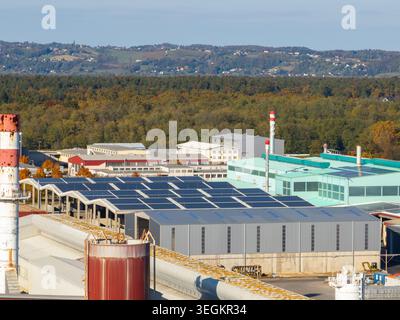 La vue aérienne capture un site industriel avec des bâtiments et des panneaux solaires entourés d'arbres et de champs par temps clair. Banque D'Images