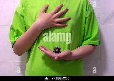 Image conceptuelle d'un adolescent tenant un modèle de virus de la plasticine avec une main sur la poitrine symbolisant une toux et une douleur thoracique. Banque D'Images