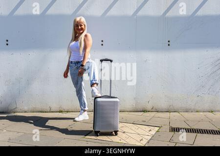 Heureuse jeune femme prête pour le voyage urbain avec valise Banque D'Images