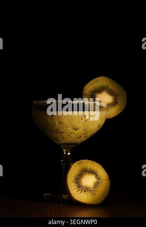 Cocktail de kiwi rafraîchissant présentant sa couleur verte éclatante et ses graines noires, servi dans un verre classique avec un bord salé et garni de kiwi frais Banque D'Images