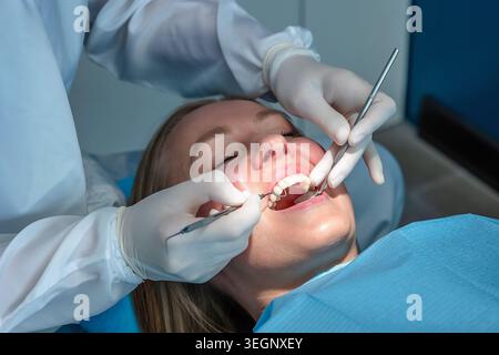 Dentiste examinant une patiente avec un miroir dentaire et une sonde lors d'un examen de prévention de routine dans une clinique dentaire moderne. Banque D'Images