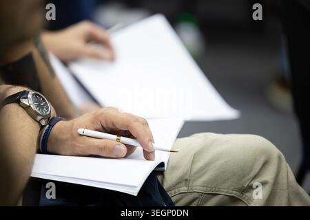 Vue rapprochée d'une personne tenant un stylo à encre blanche au-dessus d'un carnet de notes en papier ouvert lors d'un séminaire pédagogique ou d'une conférence avec un autre participant tenant un Banque D'Images
