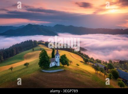 Vue aérienne de la petite église sur la colline au-dessus des nuages bas roses Banque D'Images