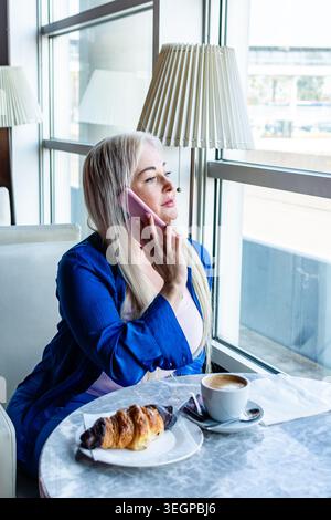 Femme faisant un appel téléphonique pendant le petit déjeuner au café Banque D'Images