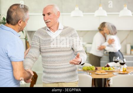 Deux hommes âgés serrant la main dans la cuisine Banque D'Images