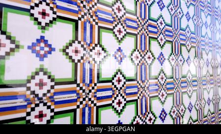 Photo en perspective d'un mur carrelé brillant présentant un motif répété de croix et de losanges. La surface décorative affiche une palette vibrante Banque D'Images