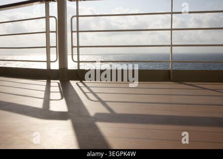 Vue paisible sur l'océan depuis un paquebot de croisière de luxe, soleil chatoyant sur la mer projetant de longues ombres sur la promenade Banque D'Images