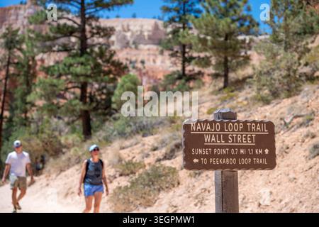 Randonneurs sur le Navajo Loop Trail marchant devant le panneau Wall Street dans le parc national de Bryce Canyon par une journée ensoleillée Banque D'Images