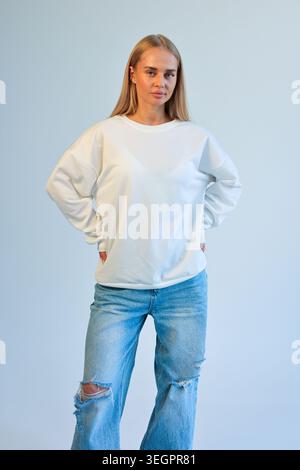 Une jeune femme habillée de façon informelle se tient elle-même dans un cadre de studio dur, établissant un contact visuel direct Banque D'Images