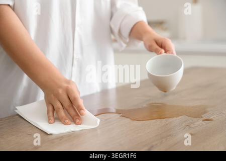 Femme essuyant le café renversé avec une serviette en papier sur la table dans la cuisine, gros plan Banque D'Images