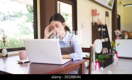 Jeunes femmes asiatiques propriétaire de petite entreprise travaillant ordinateur portable stress maux de tête problème café café entrepreneur de café Banque D'Images