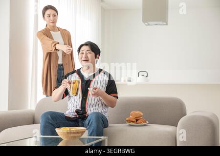 Un jeune couple se détend ensemble sur un canapé, dégustant des collations et du thé dans un salon lumineux. Banque D'Images