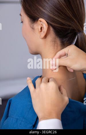 Une femme en blouse médicale bleue est traitée par acupuncture sur son cou par un professionnel de la santé dans un cadre clinique. Banque D'Images