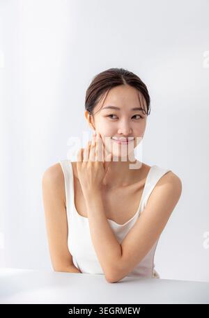 Une jeune femme asiatique la main sur la joue, souriante et regardant directement la caméra. Banque D'Images
