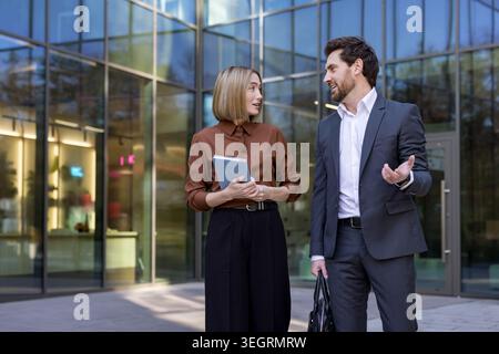 Deux collègues professionnels ont une discussion importante tout en se tenant à l'extérieur d'un immeuble de bureaux moderne, partageant des idées et collaborati Banque D'Images