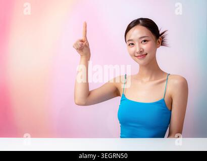 Une jeune femme dans un haut de réservoir bleu pointe vers le haut avec son index. Banque D'Images