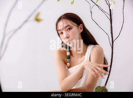 Une femme dans une robe blanche est assise près d'un arbre, sa main tendue pour toucher une branche. Banque D'Images