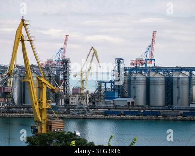 Terminal d'exportation de céréales dans le port maritime d'Odessa, Ukraine. Paysage industriel avec silos métalliques, grues de fret et infrastructures maritimes sous un ciel nuageux. Banque D'Images