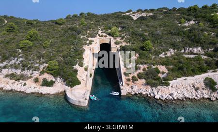 Vue aérienne de l'abri souterrain de bateau de l'armée yougoslave Potkop Parja avec des gens sur des paddleboards dans l'eau turquoise à Rogacic, Splitsko-dalmatinska Banque D'Images