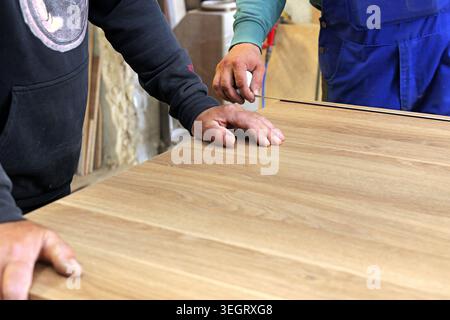 Les mains des charpentiers travaillant ensemble, mesurant avec précision une surface en bois avec une règle pour un projet de mobilier personnalisé, démontrant des compétences en travail du bois Banque D'Images
