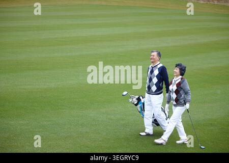 Vue latérale de couples seniors de golfeurs marchant sur le terrain Banque D'Images