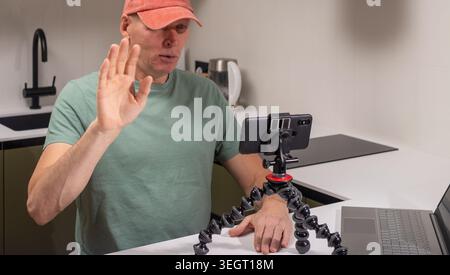 L'homme mûr lève la main saluant la caméra de smartphone pendant l'enregistrement vidéo. Un homme adulte fait des vagues lorsqu'il parle devant un appareil monté sur trépied. Accueil digi Banque D'Images