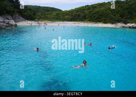 Les gens nagent et apprécient les eaux turquoises cristallines d'une crique grecque isolée Banque D'Images