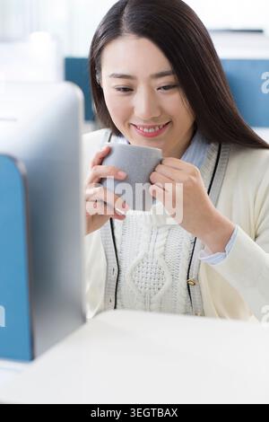 Une femme dans un cadre de bureau sourit et tient une tasse à café. Banque D'Images