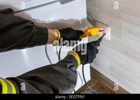 Électricien testant une prise murale avec un testeur de tension numérique pendant les travaux de maintenance électrique et de réparation à l'intérieur Banque D'Images
