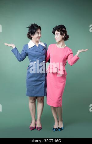 Deux femmes identiques dans des robes identiques de style années 1950 se tiennent côte à côte, les deux tenant leurs mains vides. Banque D'Images