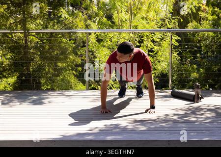 Homme effectuant push-up sur le pont en bois portant chemise athlétique rouge short noir chaussures smartwatch Banque D'Images