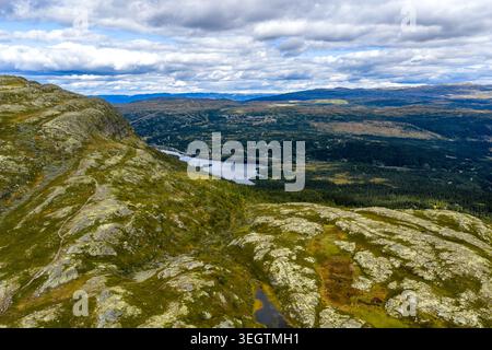 Une vaste photographie aérienne capturant un vaste paysage en couches. Au premier plan, une pente montagneuse accidentée et couverte de mousse descend vers un environnement serein Banque D'Images