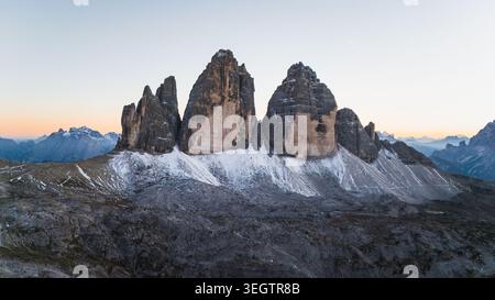 Vue aérienne des sommets emblématiques de Tre Cime di Lavaredo avec des pentes poussiéreuses de neige sous un ciel crépusculaire doux à Auronzo di Cadore, Vénétie, Italie. Banque D'Images