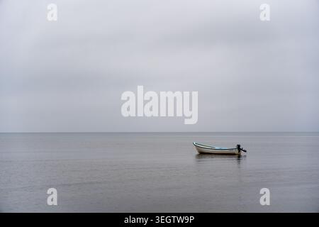 Un seul petit bateau de pêche avec un moteur hors-bord flotte paisiblement sur une vaste étendue d'eau calme. L'horizon net et propre sépare les tranquilles s Banque D'Images