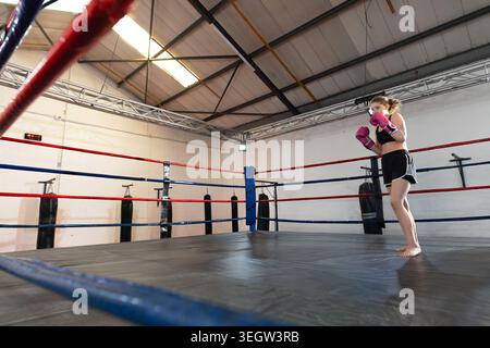 Boxeur adolescente debout sur la droite de l'anneau, pratiquant avec des gants roses, pieds nus, espace copie Banque D'Images