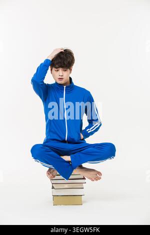 Un jeune homme est assis les jambes croisées sur une pile de livres, la main dans sa poche, avec une expression calme. Banque D'Images