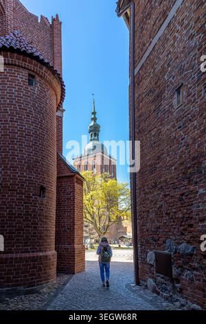 Un touriste avec un sac à dos marche dans une étroite ruelle historique en briques rouges vers le majestueux complexe de la cathédrale avec une tour baroque verte proéminente Banque D'Images
