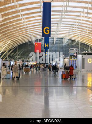 Shanghai, Chine - 11 décembre 2025 : passagers avec des bagages naviguant dans un hall moderne de l'aéroport de Pudong avec un drapeau national chinois affiché Banque D'Images