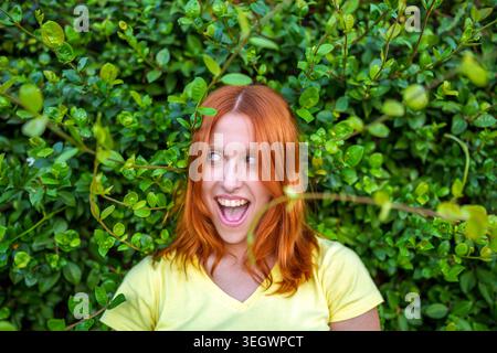 Jeune femme aux cheveux roux vifs montrant son visage expressif tandis qu'elle regarde sur le côté avec sa bouche légèrement agapée, sur fond de tanière Banque D'Images
