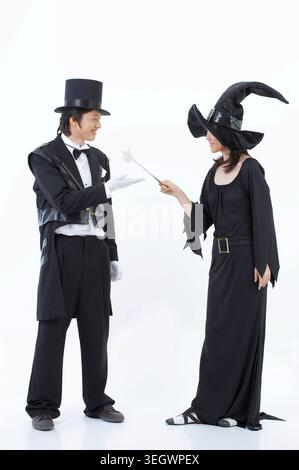 Un homme dans un chapeau de magicien et une femme dans un chapeau de sorcière exécutent un tour de magie, l'homme tenant une baguette et la femme portant une longue robe noire. Banque D'Images