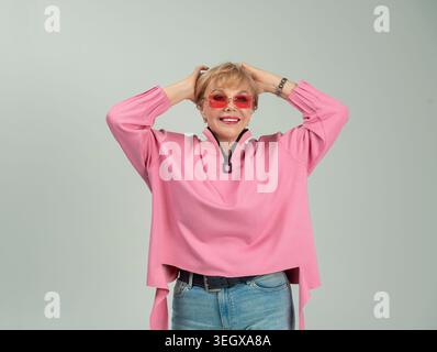 Une femme adulte, émotionnelle, espiègle, heureuse dans des vêtements roses et des lunettes avec ses mains levées Banque D'Images