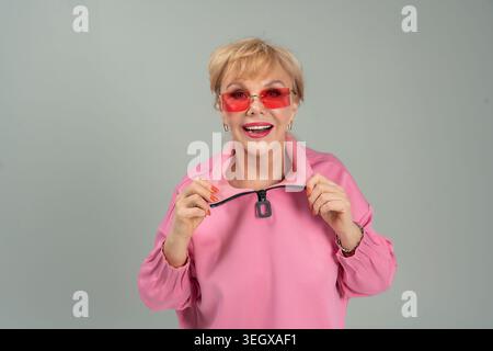 Une femme adulte, émotionnelle, espiègle, heureuse dans des vêtements roses et des lunettes avec ses mains levées Banque D'Images