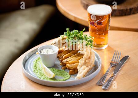 Croustillant Fish and Chips servi avec une sauce verte rafraîchissante et de la bière dans un cadre confortable Banque D'Images