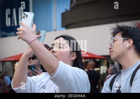 A Times Square, juste à côté de la 42e rue, un touriste asiatique prend des photos de téléphone portable avec deux mobiles. À Midtown Manhattan, mai 2026. Banque D'Images