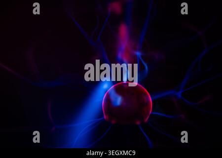 Gros plan d'un globe à boule de plasma brillant avec une lumière rouge et des rayons d'électricité d'énergie sur un fond noir Banque D'Images