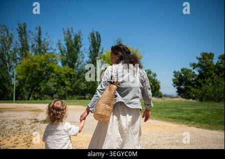 La mère et le tout-petit marchent main dans la main le long d'un chemin ensoleillé dans le parc, partageant un moment de chaleur, de soins et de loisirs en plein air en famille lors d'une somme détendue Banque D'Images