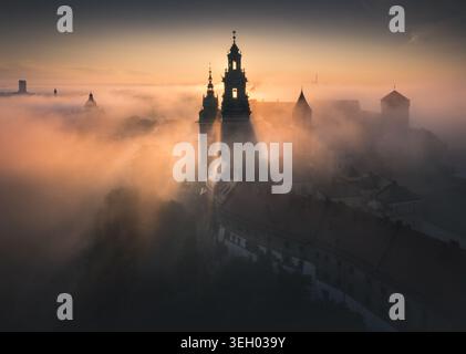Vue aérienne du château royal de Wawel et de la cathédrale enveloppés dans un épais brouillard matinal lors d'un lever de soleil doré à Cracovie, petite Pologne Voïvodie, Pologne. Banque D'Images
